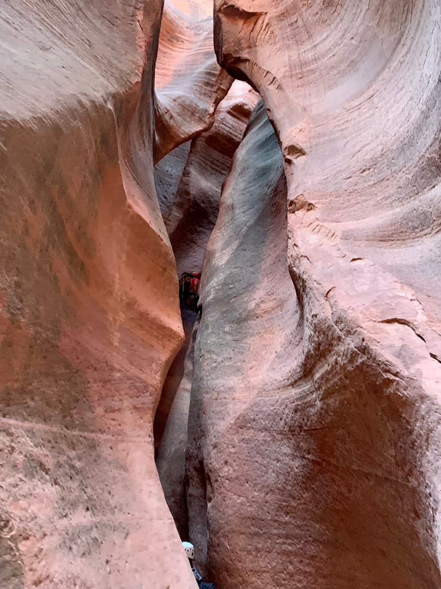 A canyoneering guide descends along a 65 foot drop in a Utah slot canyon