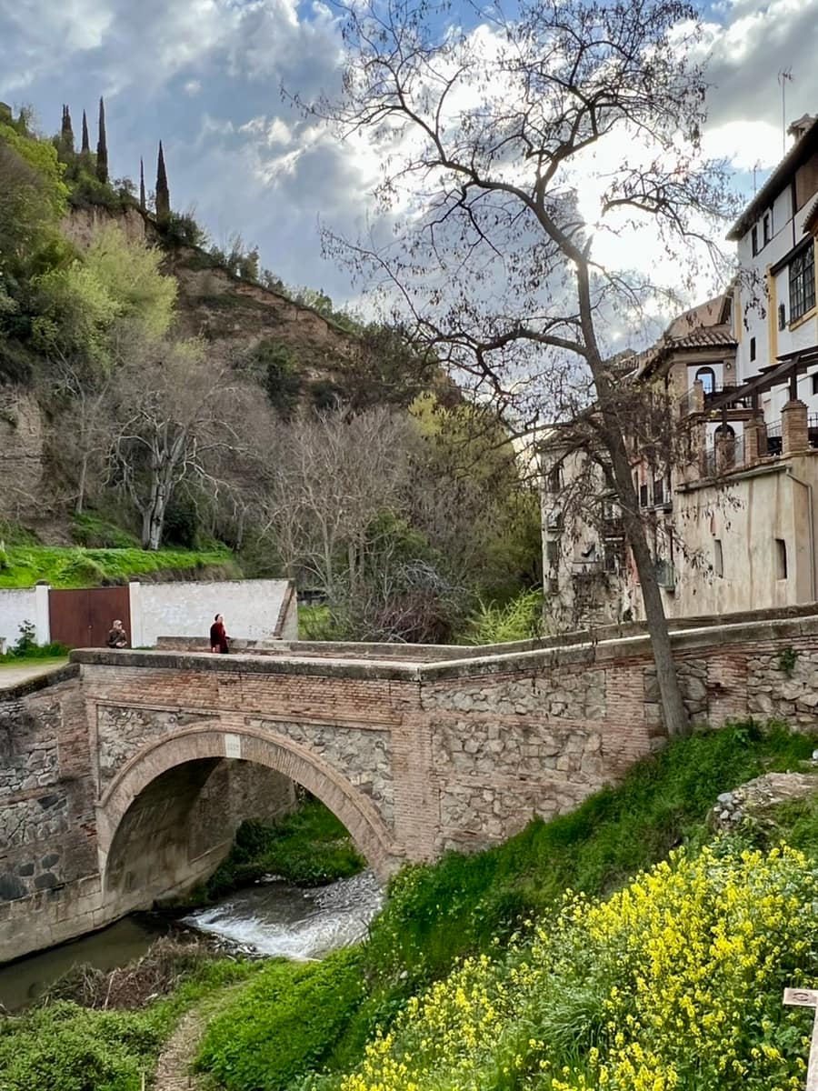 A bridge crosses the Darro river along Granada's Paseo de los Tristes