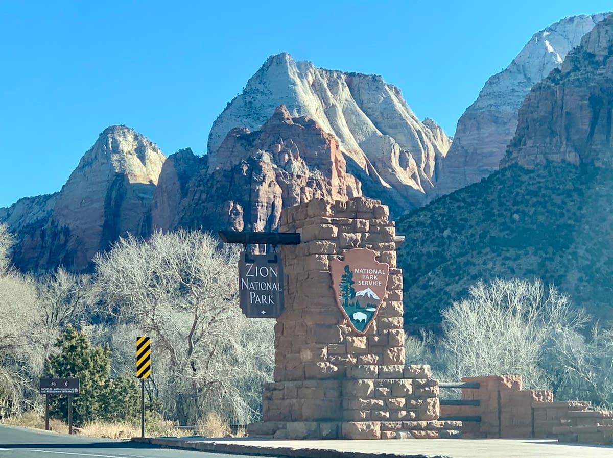 Entrance sign to Zion National Park with tall sandstone peaks in the background
